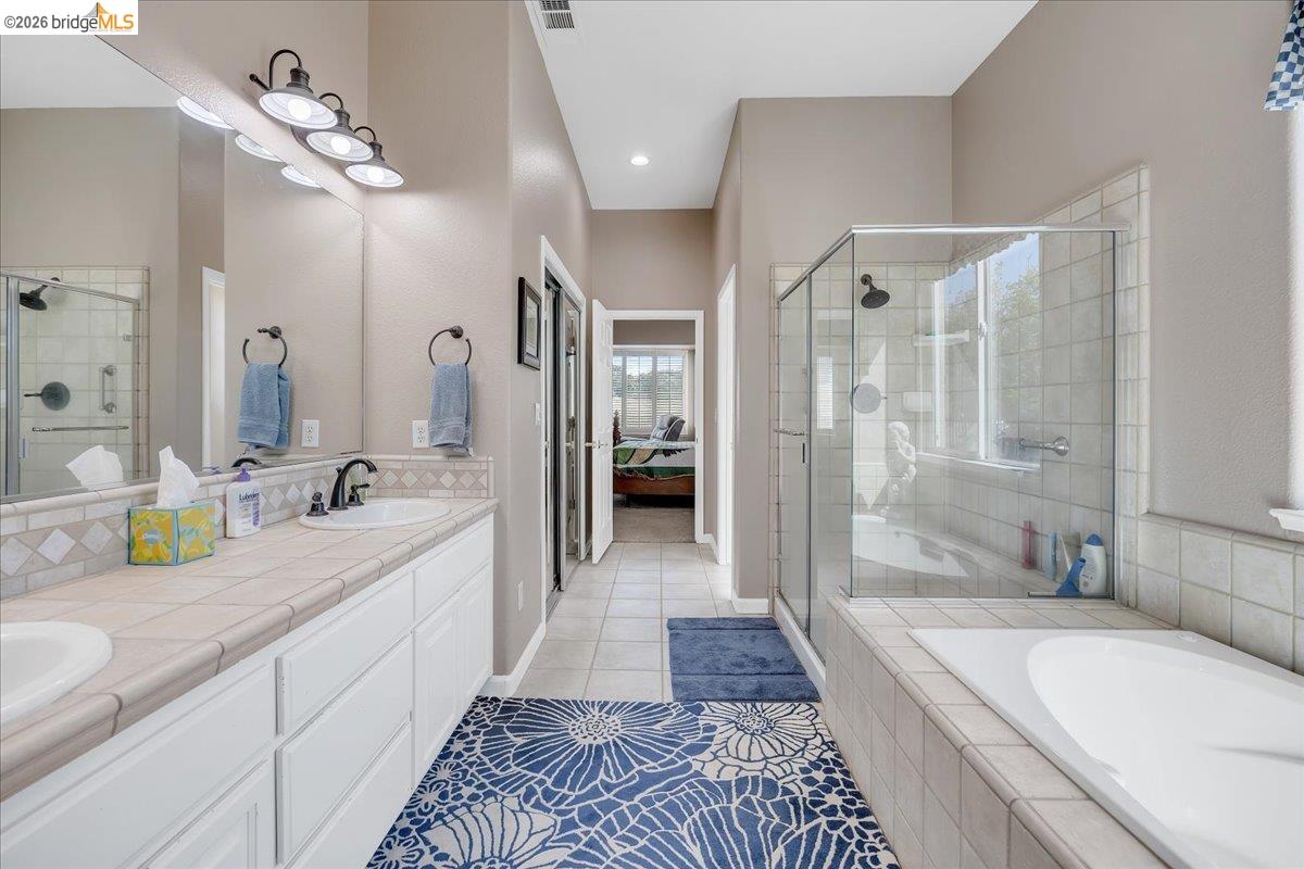 158 Rock Ridge Lane Copperopolis, CA 95228 - Photo 36 of 72 Bathroom featuring a dual-sink vanity with white cabinetry and tile countertop, a walk-in shower with clear glass enclosure, a built-in bathtub, and tile flooring