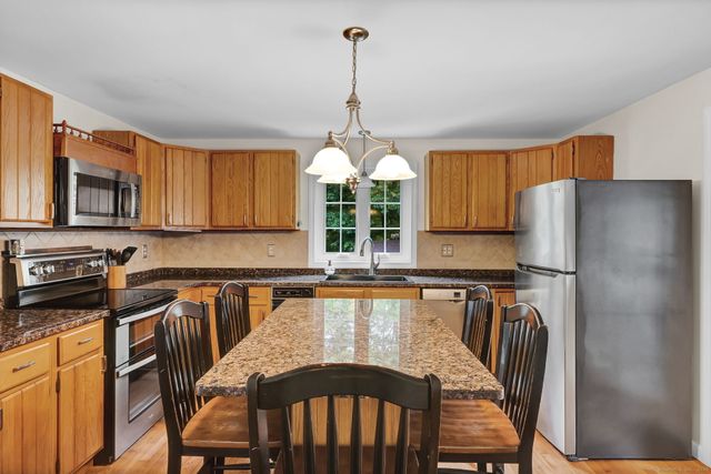 a kitchen with stainless steel appliances granite countertop a refrigerator a stove a sink dishwasher a dining table and chairs with wooden floor