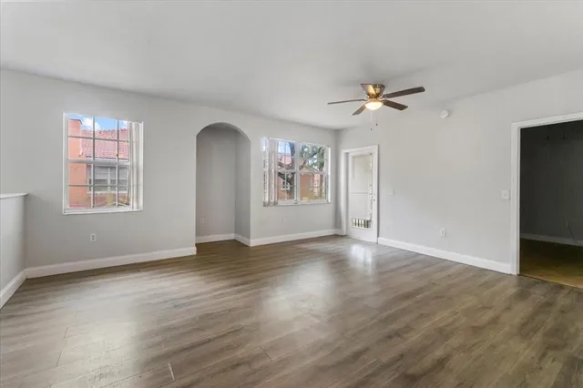 an empty room with wooden floor chandelier fan and windows