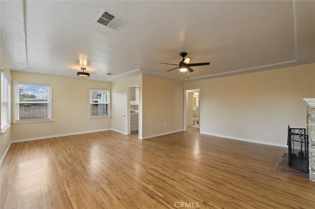 an empty room with wooden floor chandelier fan and windows