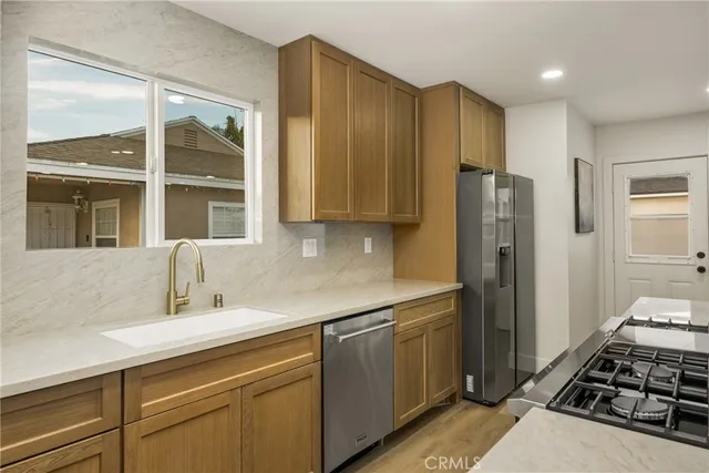 a kitchen with stainless steel appliances a stove a sink a refrigerator white cabinets and couches with wooden floor