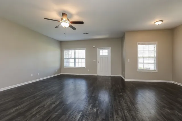 an empty room with wooden floor chandelier fan and windows
