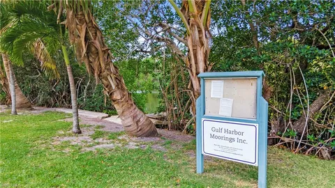 a sign that is sitting in front of a house with a tree