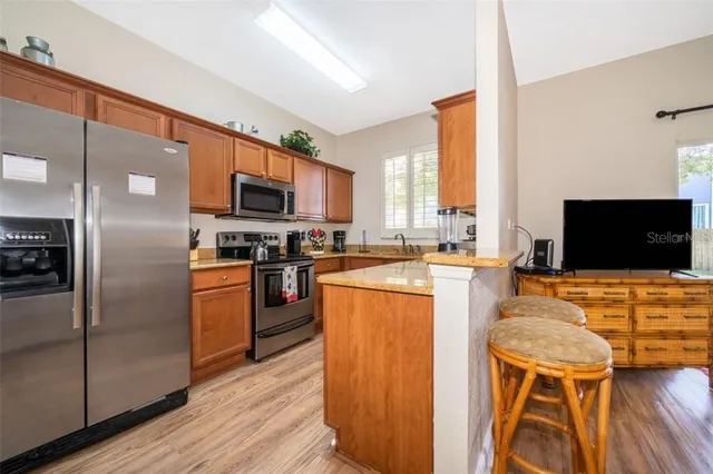 a kitchen with stainless steel appliances kitchen island granite countertop a refrigerator a stove top oven a sink dishwasher and wooden cabinets with wooden floor
