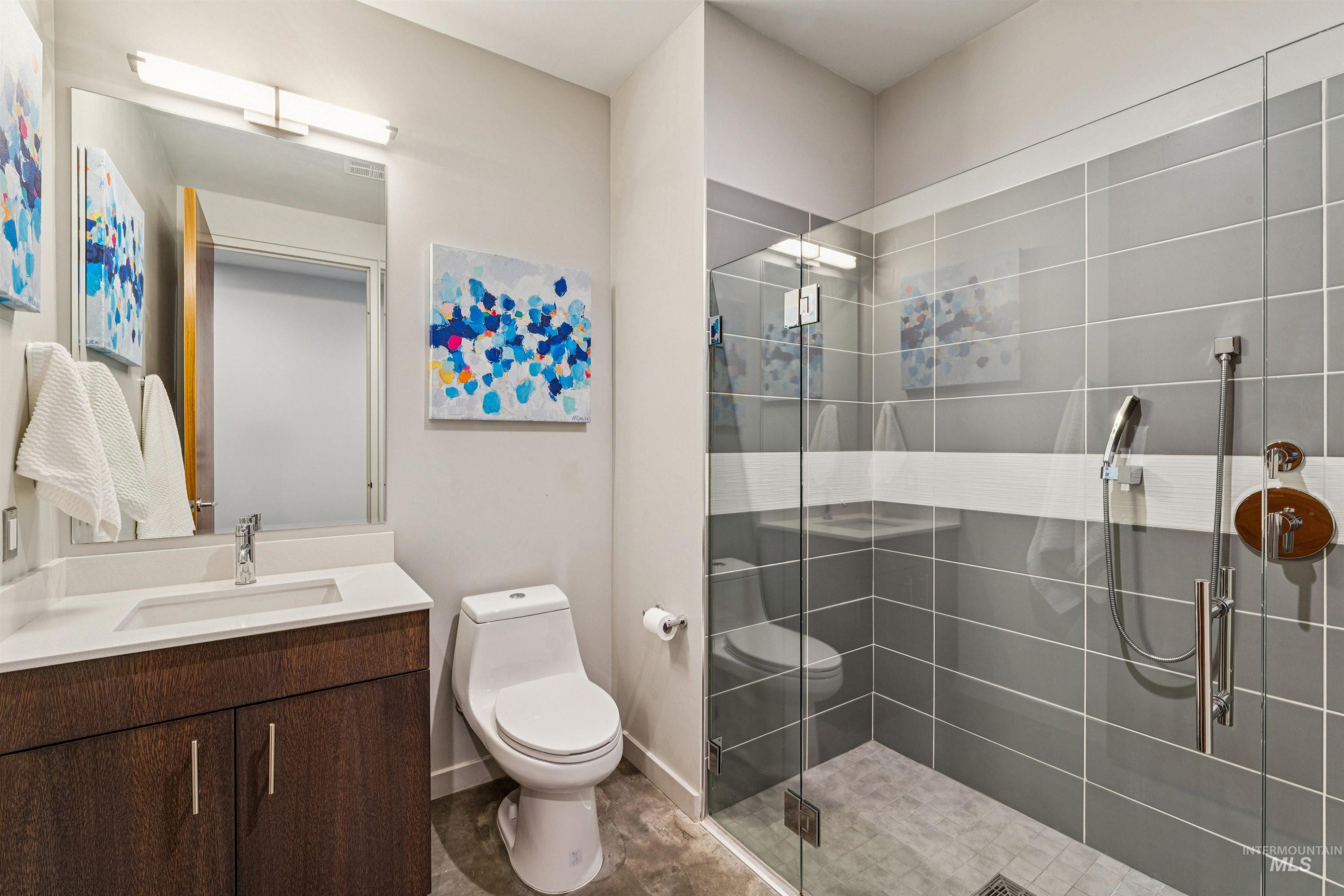 119 South 10th Street, Unit 307 Boise, ID 83702 - Photo 32 of 47 Full bathroom featuring a glass-enclosed shower with gray and white tile, a wood-finish vanity with a white countertop and undermount sink, and a mirrored medicine cabinet