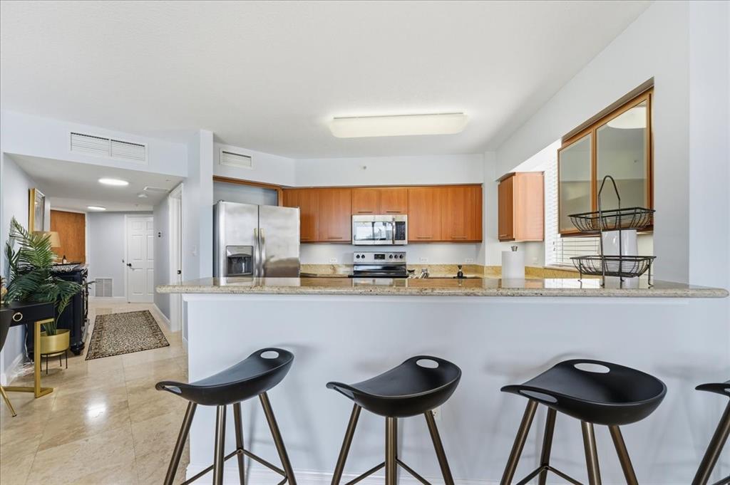 2011 North Ocean Boulevard, Unit 302 Fort Lauderdale, FL 33305 - Photo 13 of 45 a kitchen with stainless steel appliances a dining table chairs and wooden cabinets