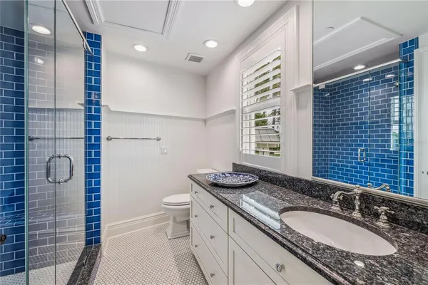 a bathroom with a granite countertop sink a toilet a mirror and shower