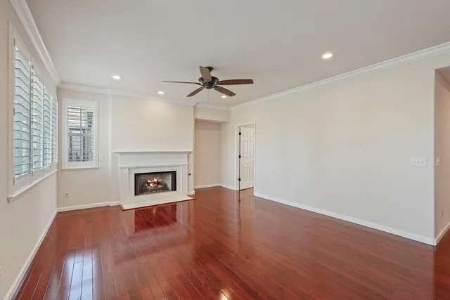 an empty room with windows a fireplace a ceiling fan and wooden floor