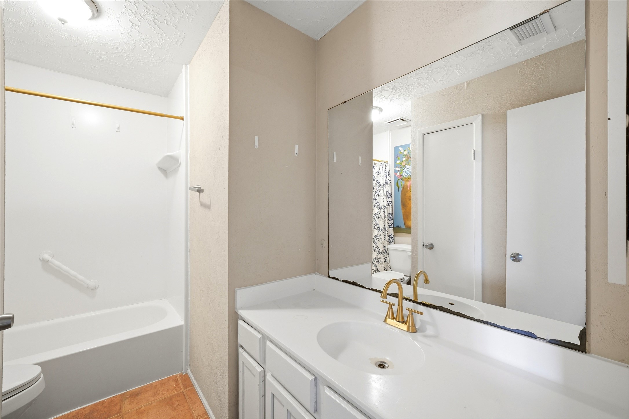 4718 Temple Bell Drive Spring, TX 77388 - Photo 32 of 50 This bathroom features a clean and simple design with a white vanity and gold faucet, a large mirror, and a bathtub with a shower. The space has neutral walls and tile flooring, offering a functional and blank canvas for personal touches.