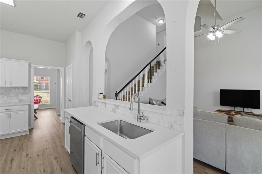 409 Springtree Road Lake Dallas, TX 75065 - Photo 15 of 40 White shaker cabinetry, light wood-finish flooring, stainless steel sink, contemporary faucet, and white countertops