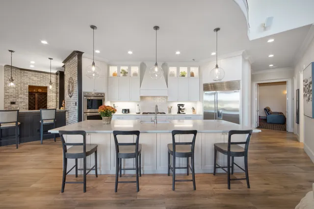 a dining hall with stainless steel appliances kitchen island granite countertop a table chairs and a chandelier