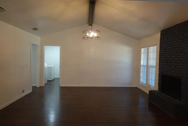 an empty room with wooden floor chandelier and windows