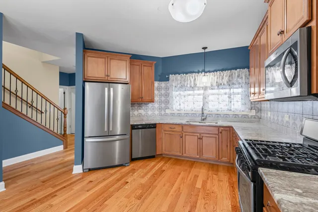 a kitchen with stainless steel appliances granite countertop a refrigerator a sink dishwasher a stove and white countertops with wooden floor