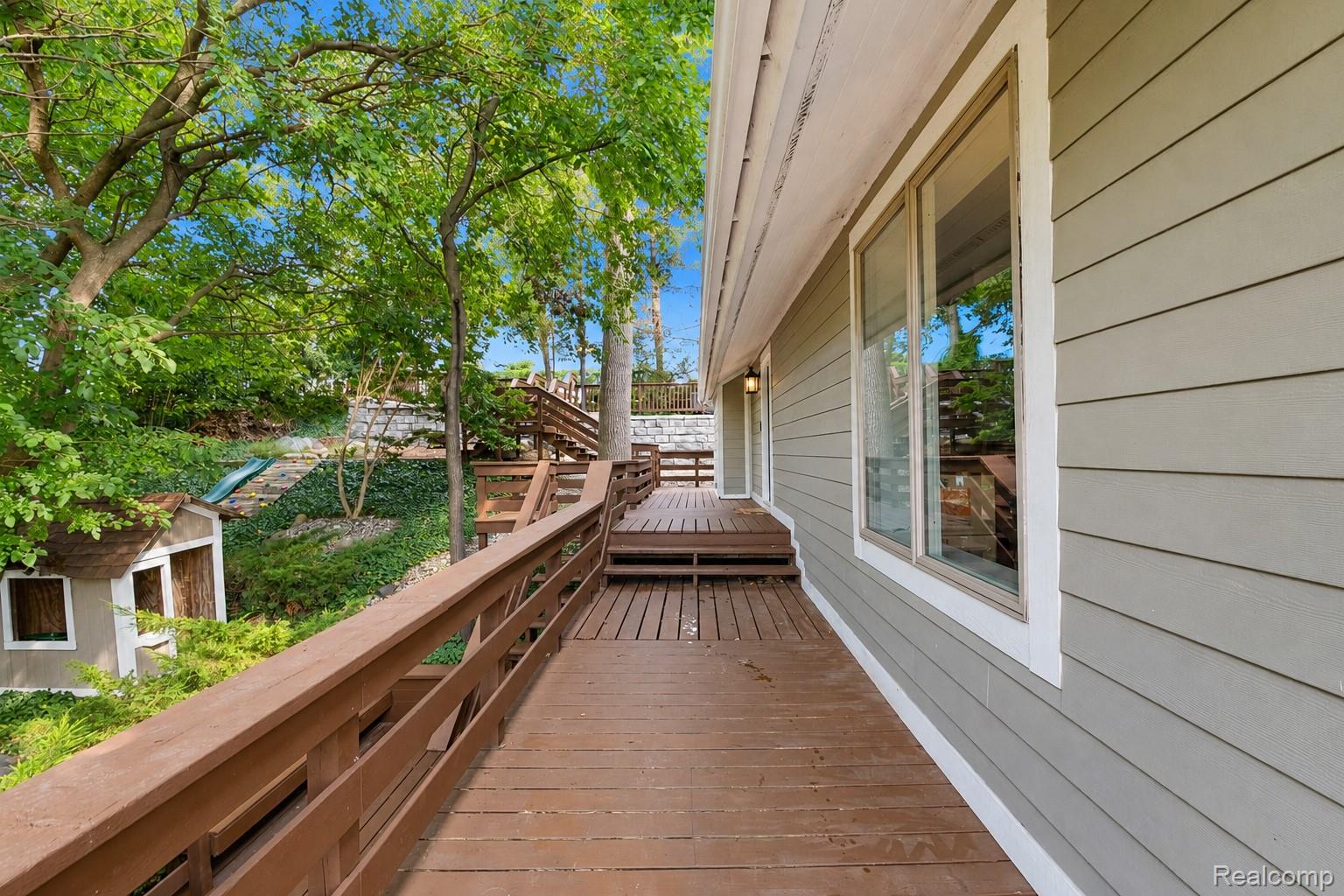 15420 Jennings Road Fenton, MI 48430 - Photo 35 of 45 Expansive wood-finish deck with integrated railing, multiple windows with white trim, and light gray siding