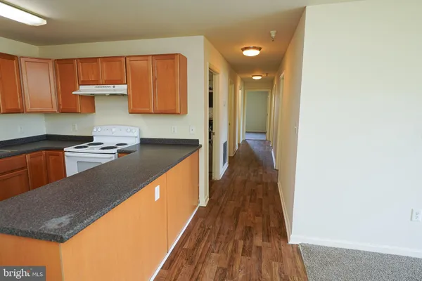 a kitchen with kitchen island granite countertop wooden cabinets a sink a stove and wooden floors