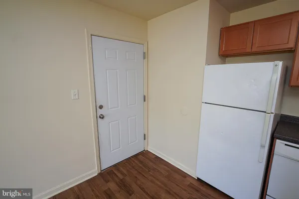 a view of a refrigerator in kitchen and an empty room with wooden floor