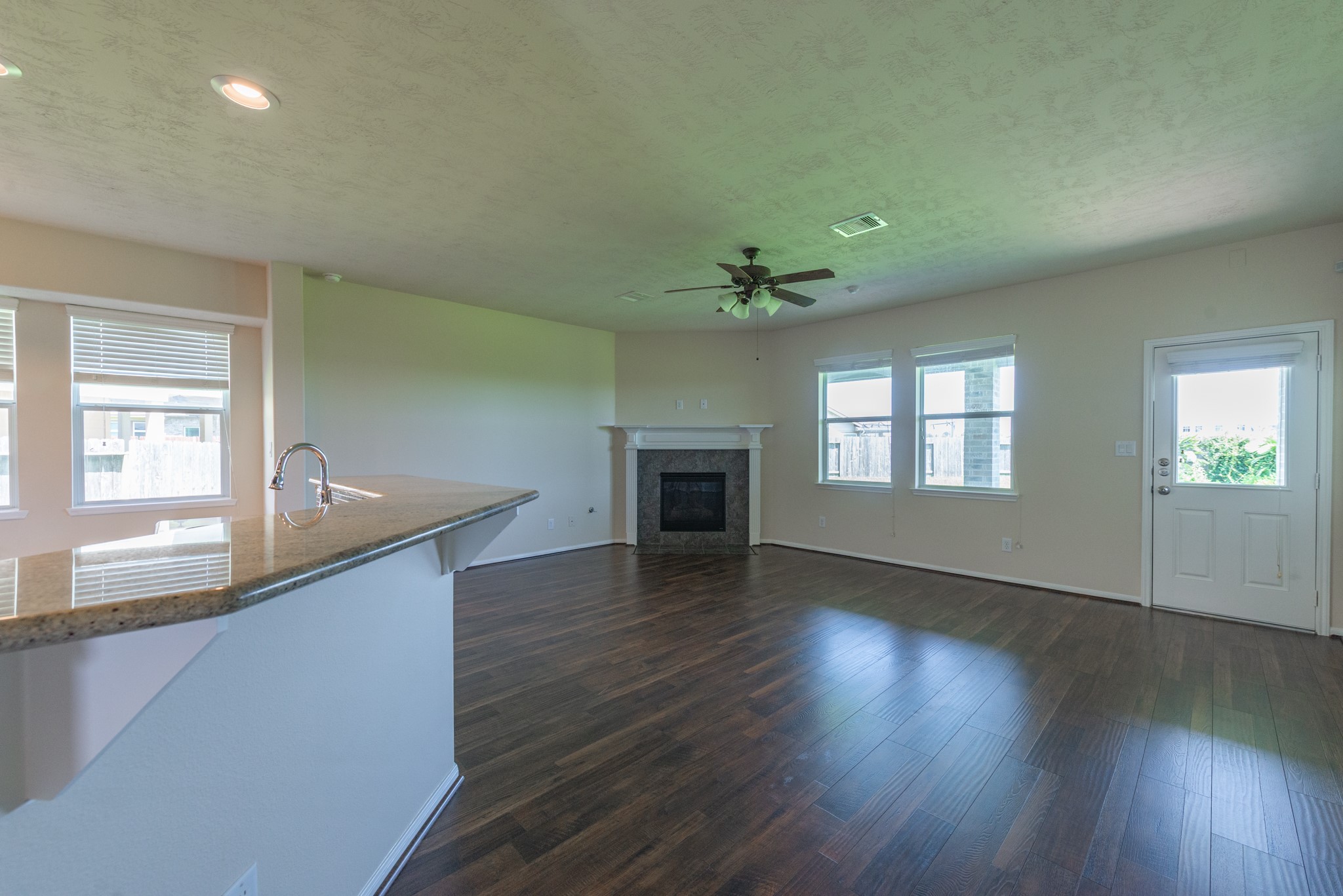 26302 Fox Ridge Lane Katy, TX 77494 - Photo 35 of 35 Large living area with rich hardwood floors, a cozy fireplace, and abundant natural light from multiple windows. The open floor plan connects seamlessly to a modern kitchen featuring a granite countertop.