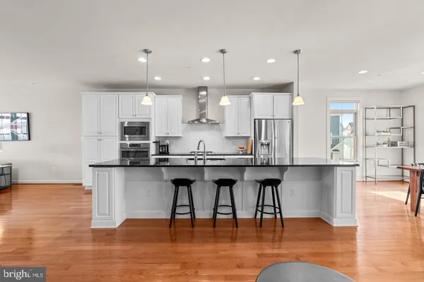 a kitchen with stainless steel appliances granite countertop a stove top oven a sink a refrigerator and white cabinets with wooden floor