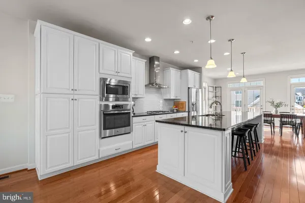 a kitchen with stainless steel appliances granite countertop a stove top oven a sink dishwasher a refrigerator and a dining table with wooden floor