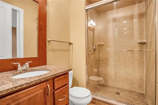 a bathroom with a granite countertop sink a toilet a mirror and shower