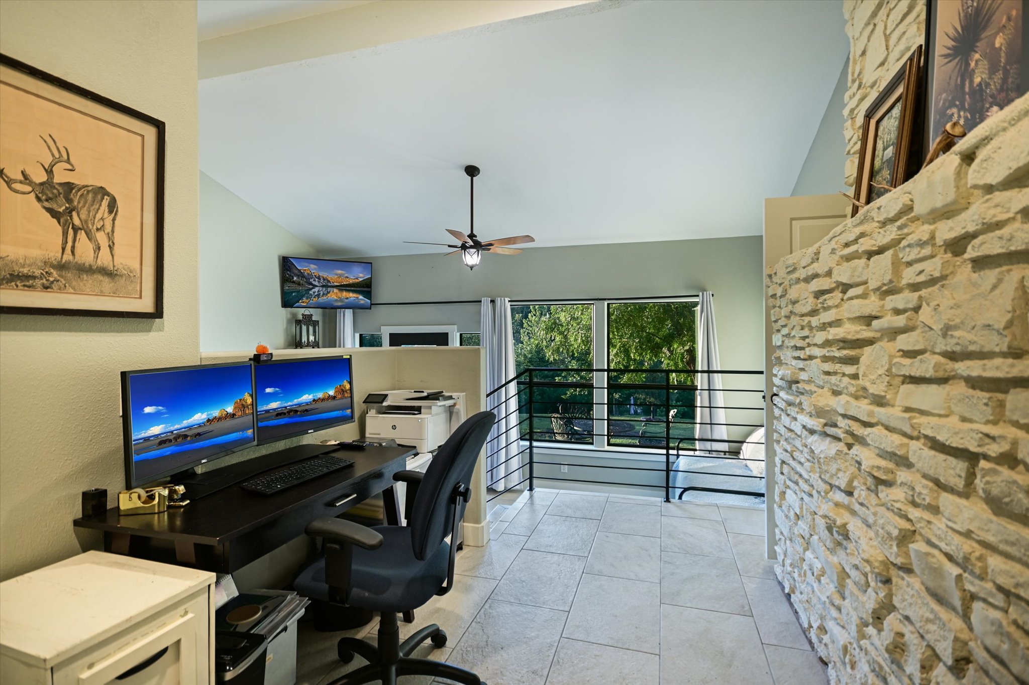 2411 Spoke Hollow Road Wimberley, TX 78676 - Photo 29 of 37 Well-lit office area with high ceilings and a view of verdant trees, featuring tile flooring and a stone accent wall.
