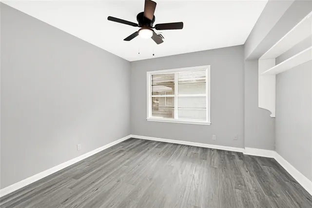 an empty room with wooden floor ceiling fan and window