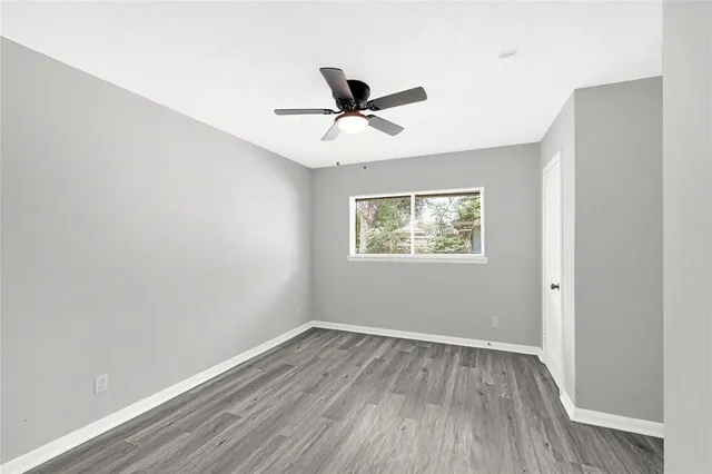 an empty room with wooden floor ceiling fan and window