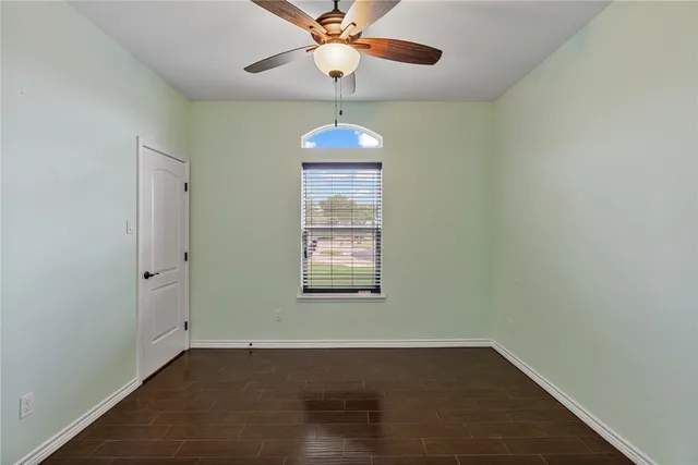 an empty room with wooden floor chandelier fan and windows
