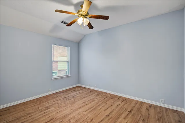 an empty room with wooden floor fan and windows