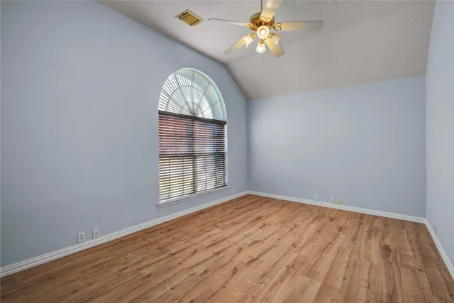 an empty room with wooden floor chandelier fan and windows
