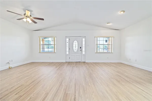 an empty room with wooden floor chandelier fan and windows