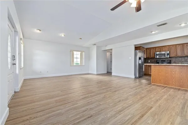 an empty room with wooden floor kitchen view and windows