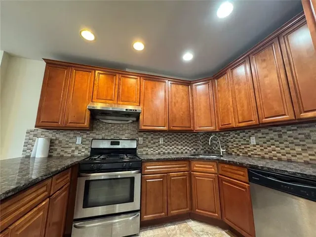 a kitchen with granite countertop wooden cabinets stainless steel appliances a sink and a window
