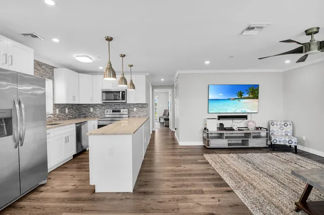 a large kitchen with stainless steel appliances kitchen island granite countertop a stove a sink dishwasher a refrigerator and white cabinets with wooden floor