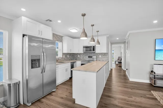 a large kitchen with stainless steel appliances kitchen island granite countertop a refrigerator a oven a island and white cabinets