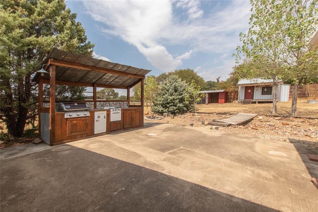 308 Sanders Road Denton, TX 76210 - Photo 26 of 31 Outdoor kitchen featuring a built-in grill, sink, and wood cabinetry with a metal roof