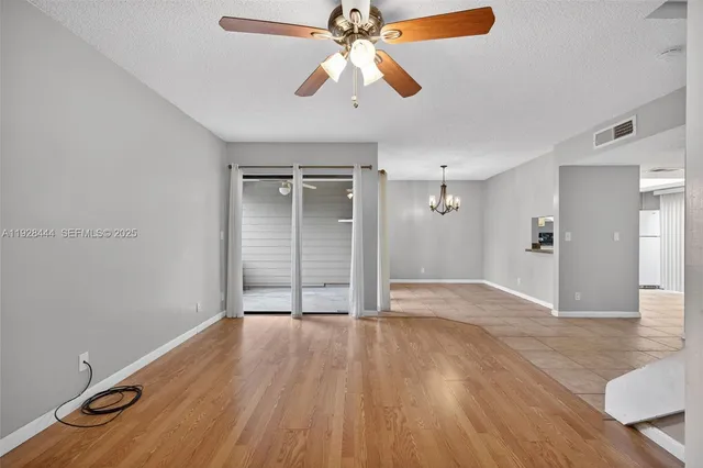 a view of an empty room with wooden floor and a ceiling fan