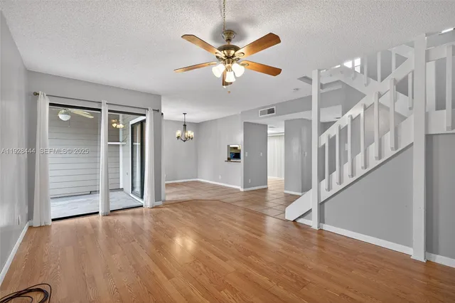 a view of an empty room with wooden floor and a ceiling fan