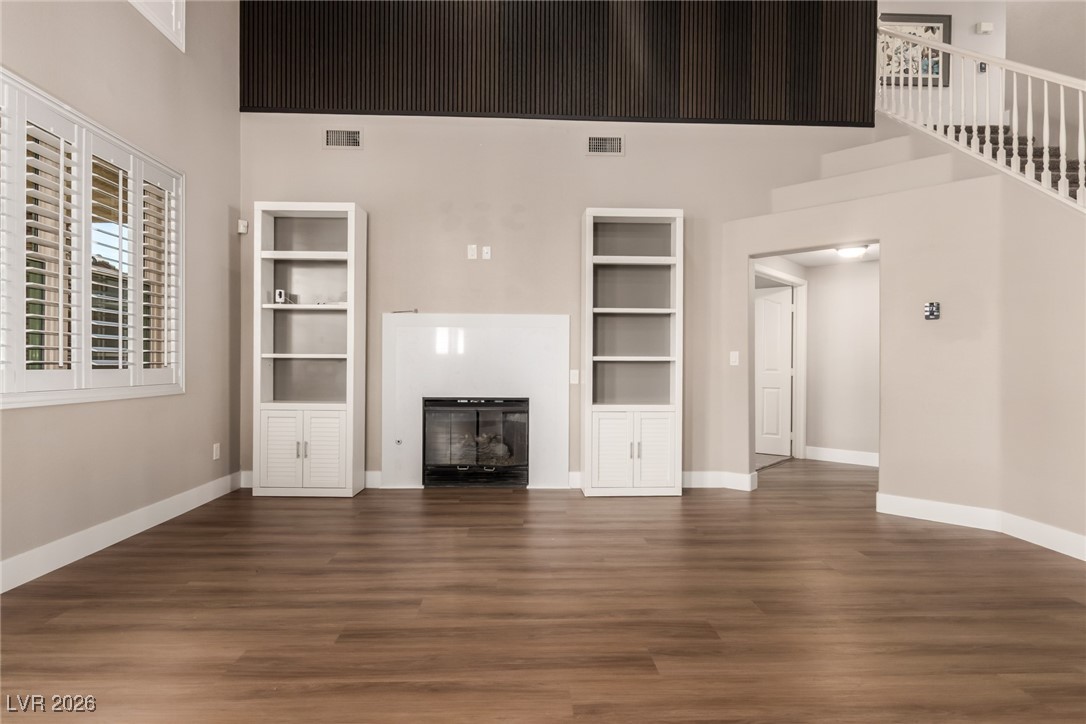 264 Pointe Ranier Avenue Henderson, NV 89012 - Photo 3 of 47 Unfurnished living room featuring built in features, a high ceiling, a glass covered fireplace, and dark wood finished floors