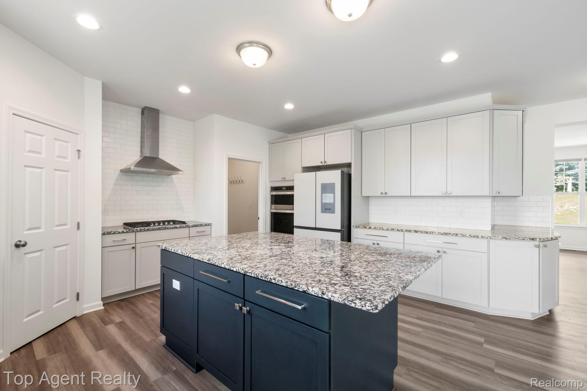 63770 Dequindre Road Washington, MI 48095 - Photo 17 of 61 Modern kitchen featuring a dark blue central island with a speckled countertop, light wood-finish flooring, white subway tile backsplash, stainless steel appliances, and recessed lighting