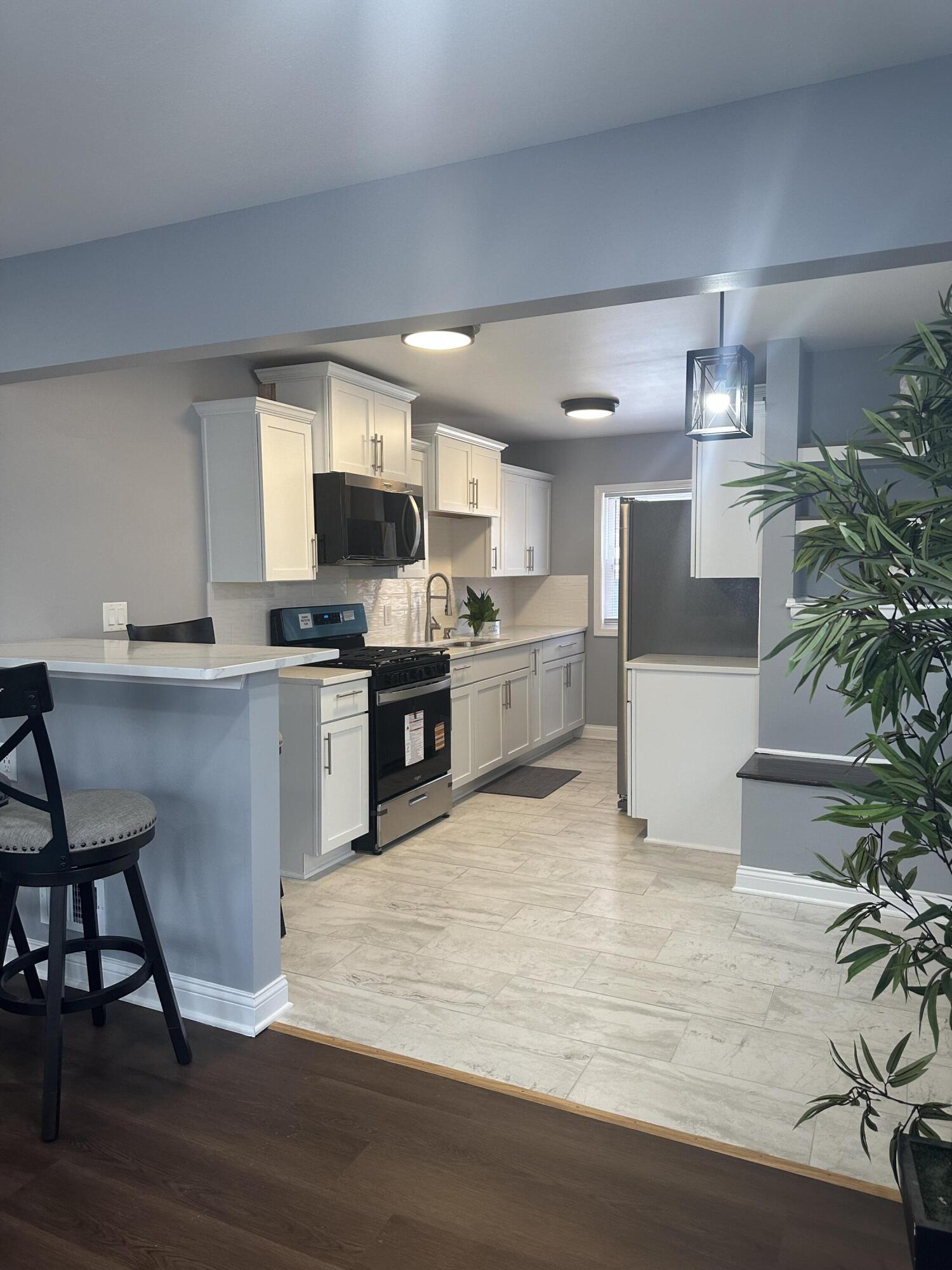 556 Gerry Street Gary, IN 46406 - Photo 5 of 21 a large white kitchen with kitchen island a potted plant on the counter and a wooden floor
