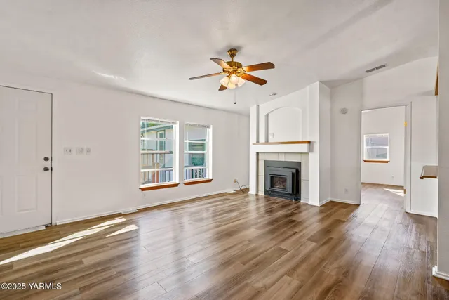 a view of a livingroom with a fireplace a ceiling fan and windows