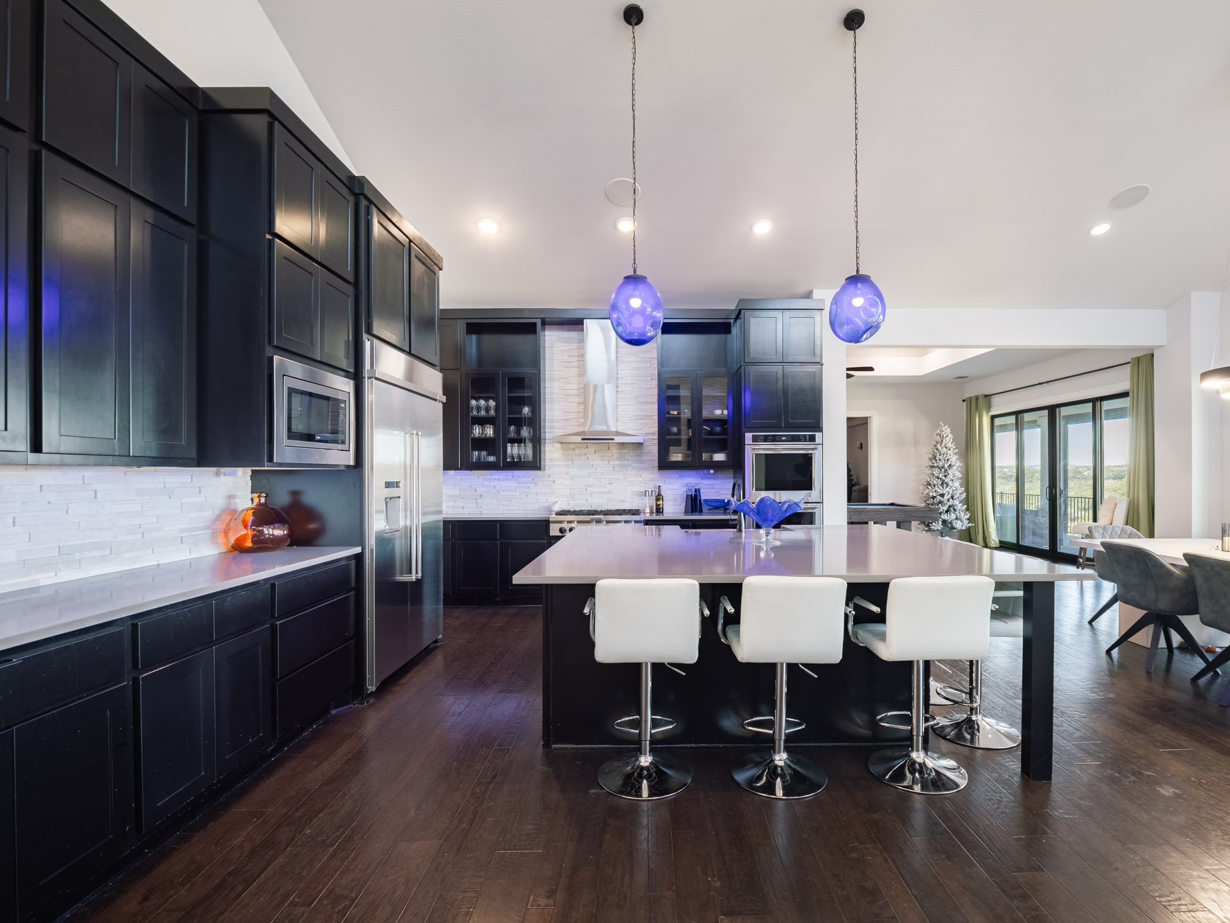 14900 Copper Ridge Lane Austin, TX 78734 - Photo 3 of 39 Kitchen featuring dark cabinets, glass insert cabinets, backsplash, pendant lighting, and a kitchen breakfast bar