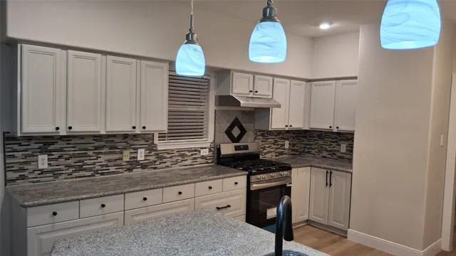 a kitchen with granite countertop a stove a sink and a white cabinets