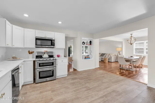 a kitchen with stainless steel appliances a stove a sink a refrigerator white cabinets and wooden floor