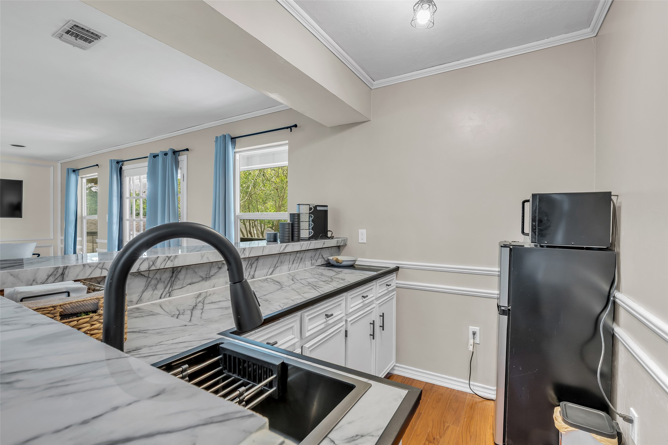 22502 Fields Lane Spring, TX 77389 - Photo 26 of 39 Apartment with Kitchen, with modern black faucet, and ample natural light from large windows with blue curtains. The space includes white cabinetry and a small black refrigerator, creating a stylish and functional environment.