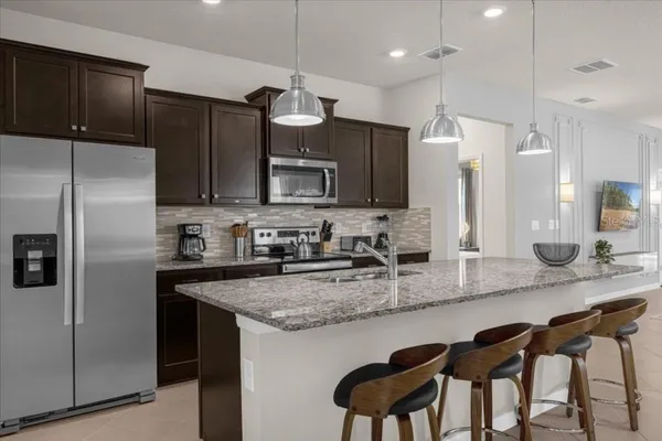 a kitchen with kitchen island granite countertop a table chairs microwave and refrigerator