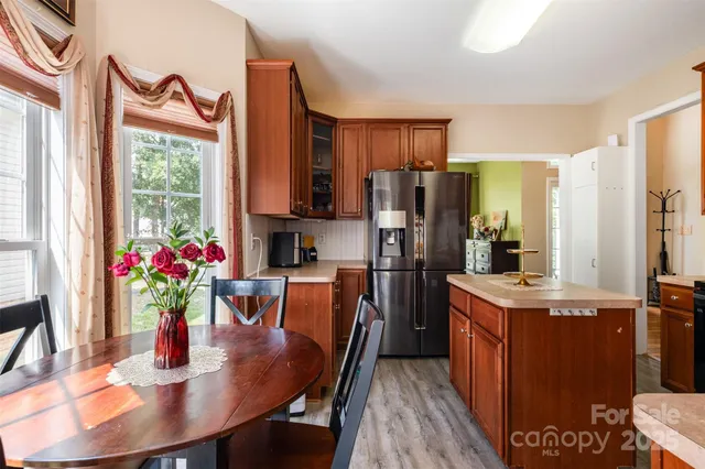 a kitchen with stainless steel appliances granite countertop a refrigerator a sink dishwasher a dining table and chairs with wooden floor