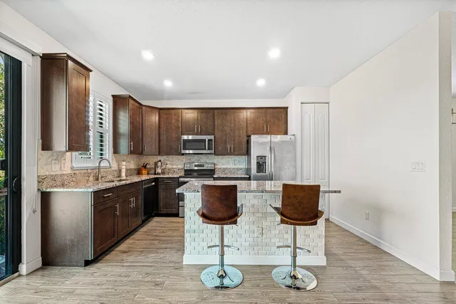 a kitchen with stainless steel appliances kitchen island granite countertop a stove a sink a refrigerator and chairs
