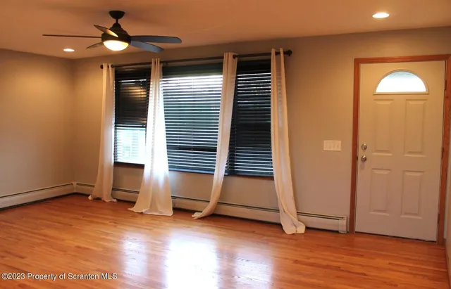 an empty room with wooden floor chandelier fan and windows